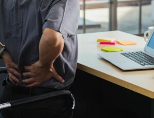 Ein Mann hält seine Hände auf seinen schmerzenden Unterrücken während er am Arbeitsplatz sitzt