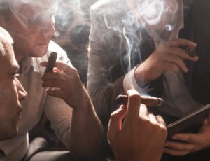 3 Männer betrachten ein Tablet und rauchen dabei eine Zigarre
