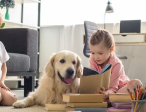 Kleine Schwestern lesen Bücher zu Hause in der Nähe eines Golden Retriever-Hundes.