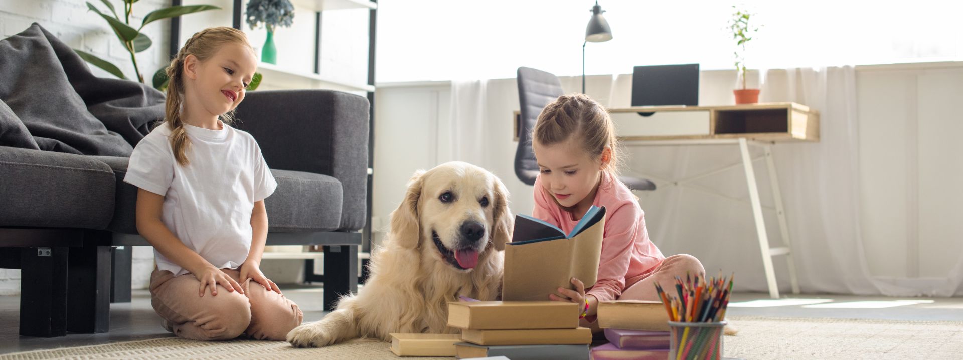 Kleine Schwestern lesen Bücher zu Hause in der Nähe eines Golden Retriever-Hundes.
