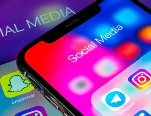 Ein Smartphone zeigt eine Nahaufnahme von Social-Media-Apps wie Instagram, Snapchat und WhatsApp. Im Hintergrund ist ein Tablet mit der Aufschrift „Social Media“ zu sehen. Die Darstellung symbolisiert die Bedeutung von Social-Media-Präsenz.