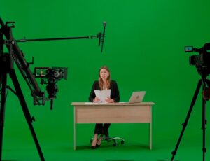 Studioaufnahme mit Greenscreen, Kamerateam und einer Person an einem Schreibtisch während einer Videoproduktion.