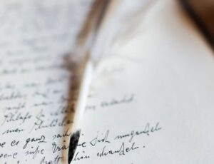 Unschärfes Foto eines offenen Buchs mit handschriftlichen Notizen auf einer Seite, darüber liegt ein schmaler Stift/Einbandrand im Vordergrund.